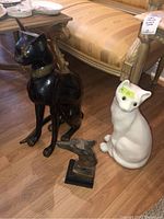 Black metal cat statue seated on floor next to white ceramic cat and dog head bust