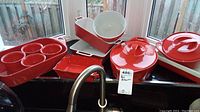 Red stoneware bakeware including large covered casserole, rectangular divided baking dish, stacked rectangular trays, and large bowl.