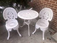 Two white cast aluminum chairs and round bistro table on concrete patio
