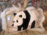 Photo of the sheepskin blanket throw laid out showing the panda design and fluffy white border on a striped upholstered surface.