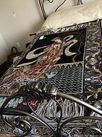 Tapestry laid flat on bed showing full design, fringe and rod across top