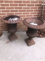 Two cast iron urn planters side by side with soil and snow at top.