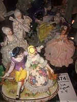 Four ceramic figurines shown together, with bright detailed 18th-century style clothing and hand-painted floral accents.