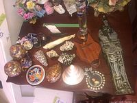 Overall view of various decorative items including cloisonné vases, shells, carvings, an Egyptian sarcophagus figure, and other collectibles arranged on a table.
