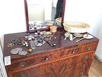 Full dresser with mirror, showing various jewelry, hand mirror, clock, and basket on top