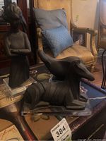 Photo showing standing female figurine and one reclining animal-like figurine both on clear plexiglass bases