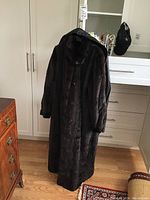 Full view of long dark brown fur coat hanging in a room, showing length and fit