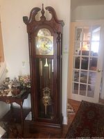 Full view of the tall wooden grandfather clock positioned against a wall beside a wooden side table with decorative items.