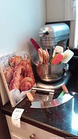 Overall view of silver KitchenAid stand mixer with attached bowl, utensils inside bowl, and 'Ultimate Bread' cookbook