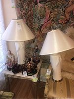 Two matching white ceramic table lamps with bird relief design placed on furniture with other decorative items and a tapestry background.