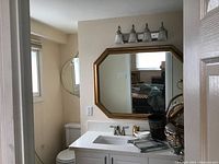 Octagonal framed mirror installed above bathroom sink with white countertop and faucet, showing size and context of use