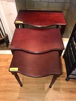 Three nesting tables stacked with front curved edges visible and size tags on top corners.