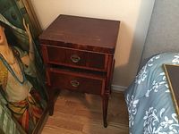 Single wooden side table with two drawers, reddish wood finish and brass drawer pulls, showing some surface wear and scratches on top