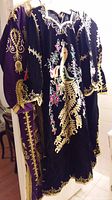 Three traditional velvet dresses shown hanging, featuring gold embroidery and ornate patterns in black and purple velvet fabrics.