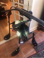 Photo of a black Nexus walker with three wheels, padded seat, brakes, and a small storage bag.