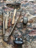 Full set including barbecue utensils and remote temperature monitor with probe shown on a patterned fabric.