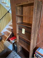 Wooden bookcase standing in basement with five shelves. Books visible on some shelves but not included in sale.