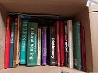Box of diverse coffee table and reference books, showing titles on spines such as antiques guide, natural healing encyclopedia, dictionaries, and easy roses.