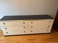 Front view of large 6 drawer dresser showing white drawer fronts with silver square handles and black top and sides.