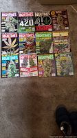 Twelve cannabis culture magazines laid out on floor, including High Times and Garden Culture editions with illustrated cannabis plants on covers.