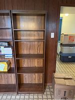 Wooden shelving unit standing upright indoors, empty, showing wood grain finish and scratches.