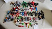 Full lot of over 50 assorted action figures, robots, and weapons from multiple toy lines on a beige surface.
