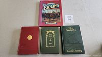 Four vintage and antique Rudyard Kipling books laid flat, showing front covers including a colorful dust jacket on one book