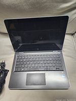 Open HP Pavilion laptop front view showing keyboard, screen off, power cord to left.