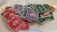 Close-up photo showing an assortment of King George VI stamps in red, purple, green, and blue, some with postmarks.