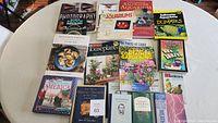 Top-down photo of 18 assorted reference books arranged on a white table, topics include gardening, photography, aquariums, cooking and bird guides