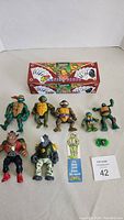 Photo showing 8 Teenage Mutant Ninja Turtles action figures, a bookmark, and a box of 12 unopened playing card packs.