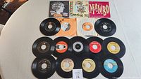 Full display of 16 vinyl 45 rpm records arranged on a flat surface with some original sleeves and album covers visible