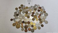 Full assortment of approximately 100 world coins laid out flat on neutral surface, showing variety in size and metal tone.