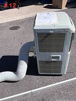 Full view of Sears portable air conditioner unit with attached flexible vent hose, shown outside on asphalt surface.