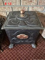 Front angle of matte black coal scuttle with brass accents and feet, showing detailed surface patterns and brass knob on lid