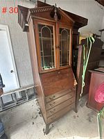 Full view of the antique wood upright writing desk showing its height and shape including pediment top and base drawers