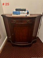 Front view of mahogany finish console showing the drawer with brass ring handles and single cupboard door. Books rest on top of the console.