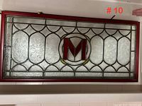 Full view of rectangular stained glass window panel with red 'M' monogram in wood frame