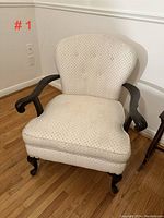 Front angled view of Queen Anne style upholstered armchair with cream diamond-pattern fabric, wooden arms and cabriole legs on hardwood floor.
