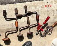 Three large ratcheting braces and two small hand drills laid on concrete.