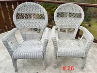 Two white wicker high back outdoor armchairs placed side by side on a concrete patio, showing full front view and condition.