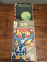 Photo showing both Batman comics 667 and 732 stacked vertically on a wooden table, both bagged.