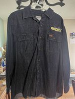 Dark blue Carhartt long sleeve denim shirt showing front featuring two chest pockets, one with button flap and Carhartt logo patch.