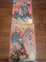 Two Batman comic books, Knightfall issues 1 and 12, bagged and displayed on a table, showing front covers with Batman illustrations.