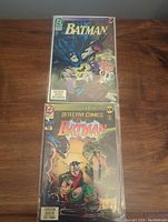 Two Batman comics, Knightfall #9 on top and Detective Comics #4 on the bottom, both bagged and displayed on a wooden surface.