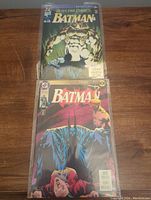 Photo showing two Batman Knightfall comic books, issues 3 and 18, both sealed in plastic bags and resting on a wooden surface.