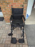 Front view of a black folding wheelchair showing the seat pad, armrests, footrests, and locking back wheels.
