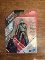 Front view of the unopened GI Joe Snake Eyes action figure in original packaging showing the figure, packaging with Snake Eyes branding and safety warnings.