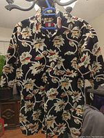 Front view of Hawaiian style shirt with large floral pattern in cream and white on black background, short sleeves and collar visible.