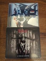 Front covers of two Slipknot CDs: Iowa with goat design on top and .5: The Gray Chapter with skeleton figure on bottom